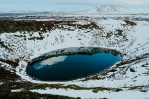 A blue lake sits in a snow-covered volcanic crater.